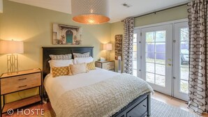 Een slaapkamer met een bed, nachtkastjes, een wandlamp, een decoratieve spiegel en een glazen schuifdeur naar een buitenruimte.