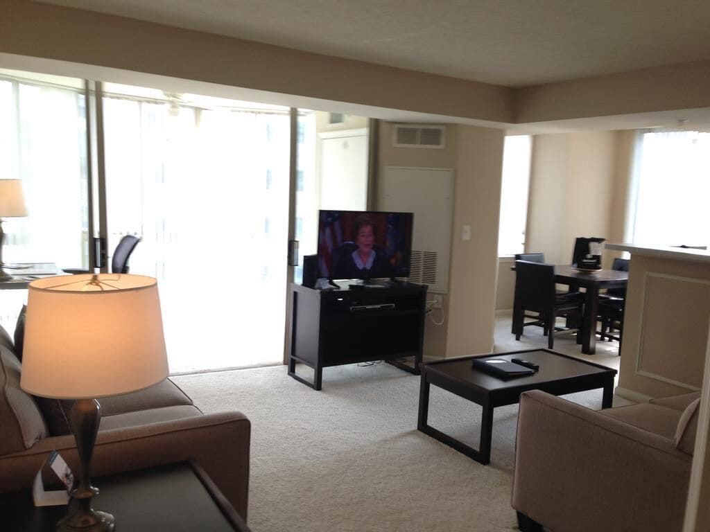 A living room with a sofa, a coffee table, a TV, and a dining area with chairs and a table.