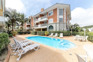 A pool area with lounge chairs and a hot tub, surrounded by a multi-story building with balconies. - Apto c/ churrasq. 2 suítes 900m da praia VDI208 (Florianópolis)