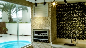 A bathroom with a glass shower enclosure, a built-in sink, and a decorative wall with a leafy pattern. - Apto de luxo em Jurerê internacional REN002 (Florianópolis)