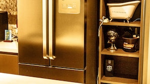 A kitchen with a stainless steel refrigerator, a wooden countertop, and a shelf with various items including a bathtub, a statue, and a bottle of Jack Daniel's whiskey. - Apto de luxo em Jurerê internacional REN002 (Florianópolis)