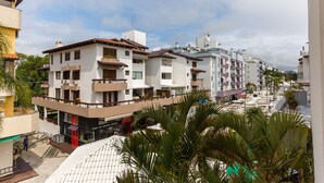 Un edificio residencial de varios pisos con balcones, un espacio comercial en la planta baja y un patio empedrado con palmeras.