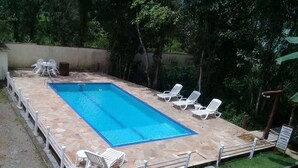 Una piscina rectangular con solana empapelada, rodeada de sillas reclinables blancas y una pequeña mesa.