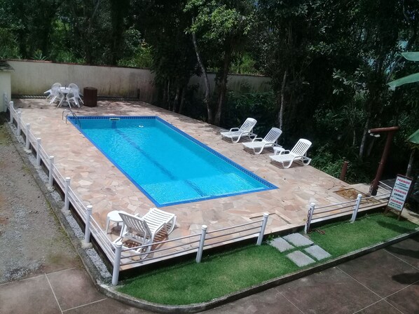 Una piscina rectangular con solana empapelada, rodeada de sillas reclinables blancas y una pequeña mesa.