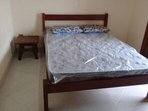 Una cama individual con estructura de madera, cubierta con un protector de colchón de plástico y dos almohadas con estampado de leopardo.