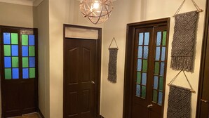 A hallway with a brown door, a green and blue stained glass window, a hanging macrame wall decoration, and a geometric light fixture. - Vintage Home near Larcomar (Urb Cercado de Miraflores)