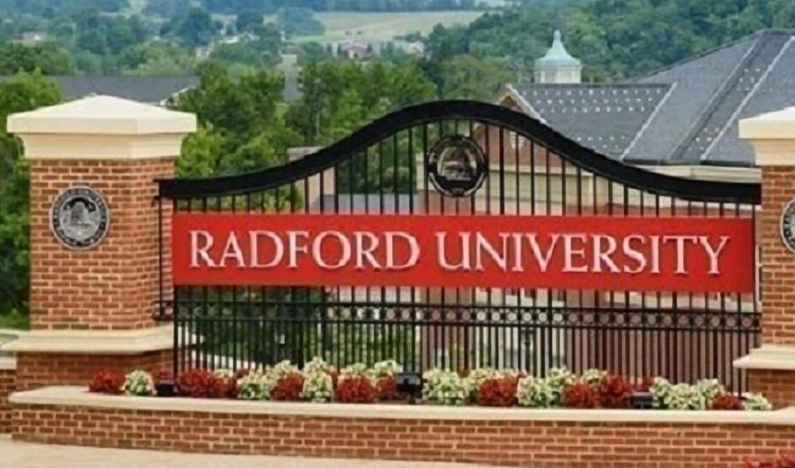 Una entrada con reja y un cartel que dice "Radford University" sobre un muro de ladrillo.
