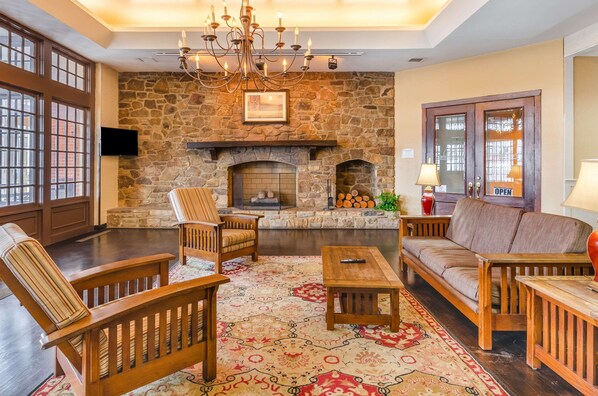 A cozy living room with a stone fireplace, wooden furniture, and large windows.