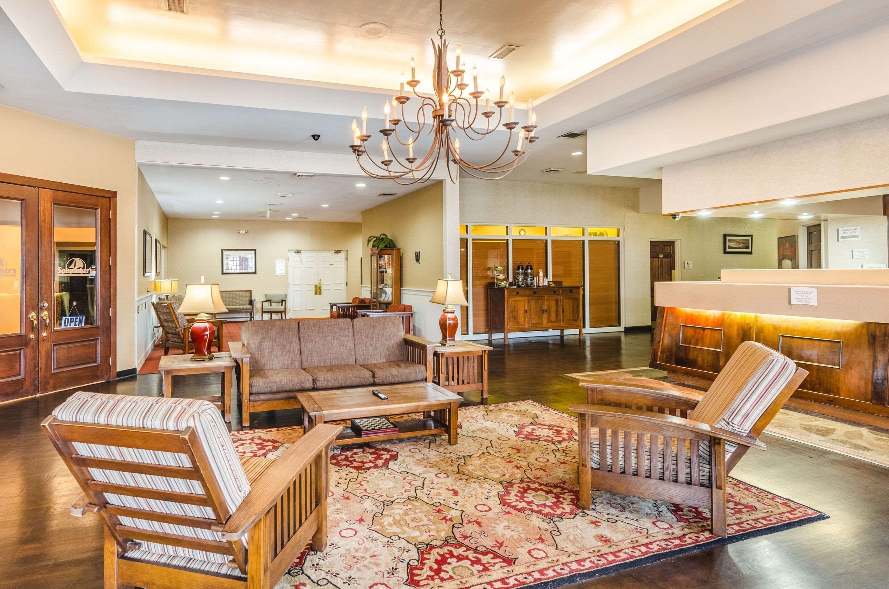 A spacious lobby with a chandelier, wooden furniture, and a patterned rug.
