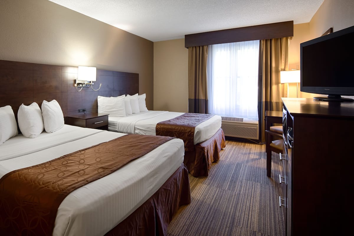 Ein Hotelzimmer mit zwei Betten, einem Schreibtisch, einem Fernseher und einem Fenster mit Vorhängen.