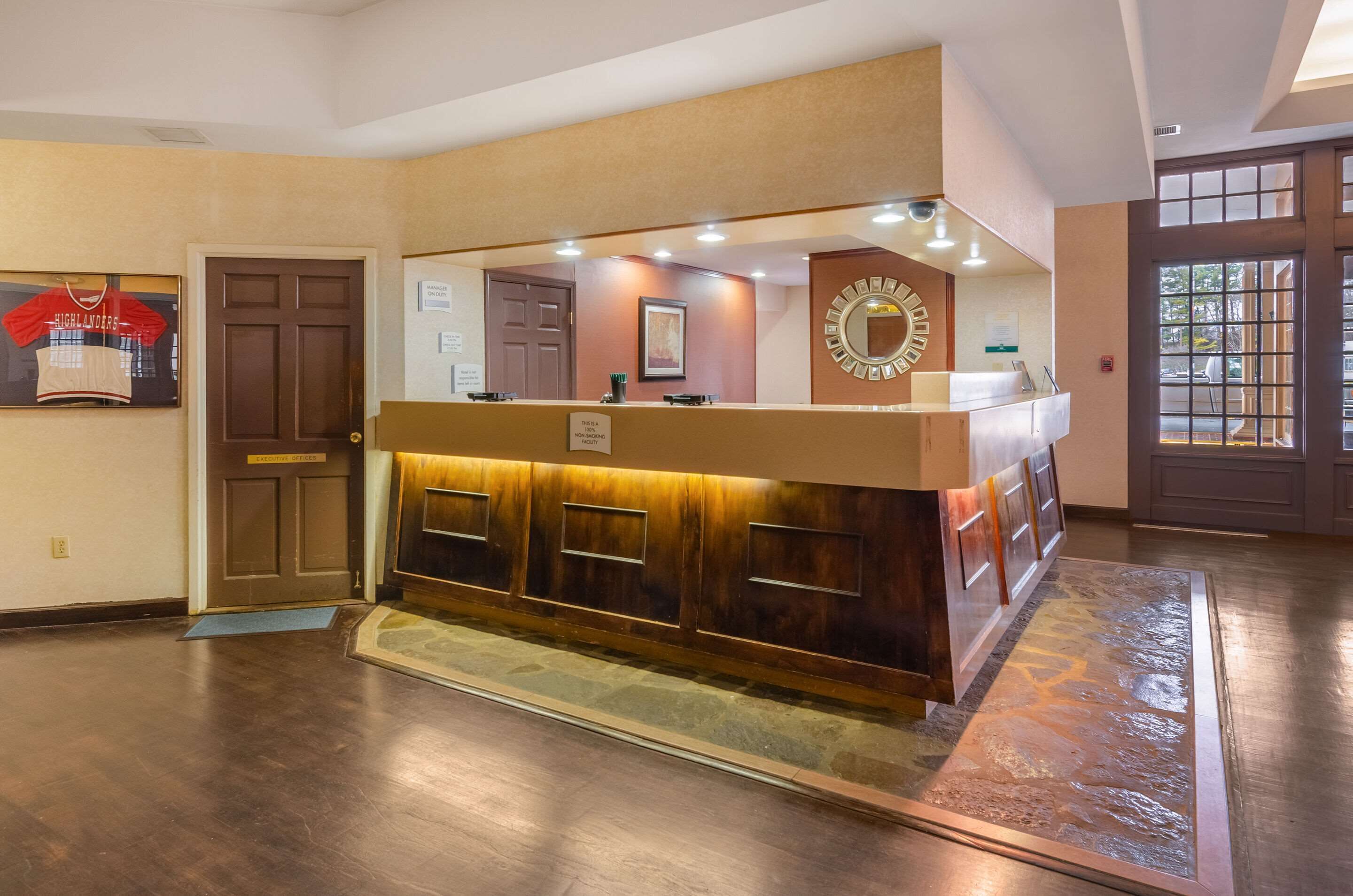 A reception desk with a wooden finish, a mirror above it, and a framed jersey on the wall.