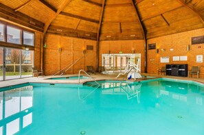 An indoor swimming pool with a wooden ceiling, brick walls, and clear glass doors leading outside.