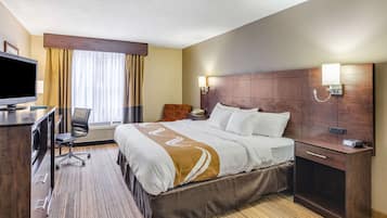 Habitación de hotel con cama, mesita de noche, escritorio con silla, televisor y ventana con cortinas.
