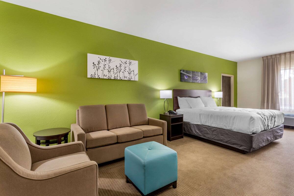 A hotel room with a green wall, a bed, a sofa, a small table, and a lamp.