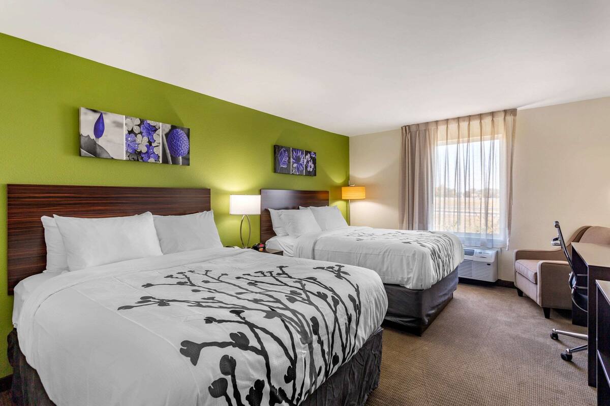 A hotel room with two beds, a desk, a chair, and artwork on the walls.