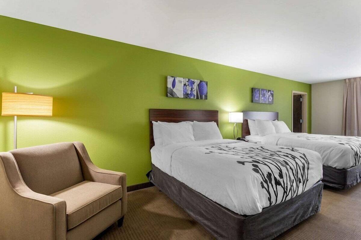 A hotel room with a green wall, two beds, a sofa, and artwork.