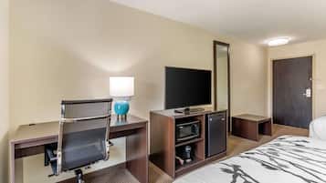 Quarto de hotel com uma cama, uma mesa com cadeira, televisão, micro-ondas, um pequeno armário e uma porta.