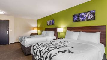 A hotel room with two beds, a green accent wall, and floral artwork.