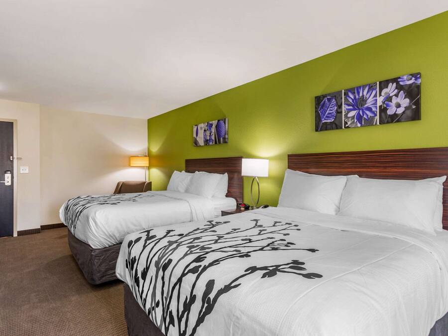 A hotel room with two beds, a green accent wall, and floral artwork.