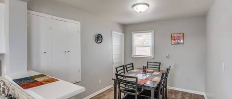 A dining area with a table and chairs, a clock on the wall, and a sign that says "HOME WHERE VINE IS".