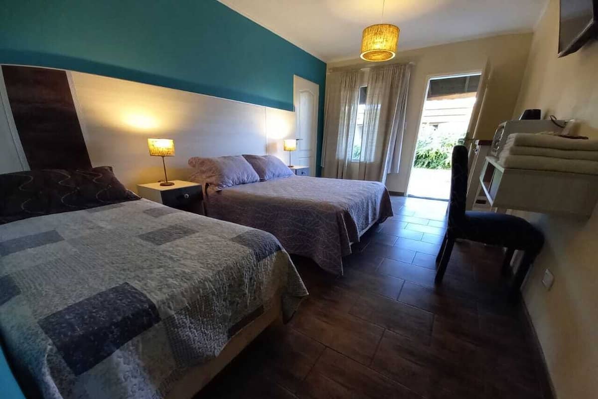 Ein Hotelzimmer mit zwei Betten, einer Sitzecke mit einem Sessel, einem Fernseher und einem Fenster mit Vorhängen.