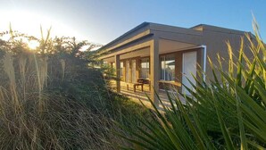 A modern house with a covered porch and a bench, surrounded by tall grass and trees. - Altos de Adonai (Lonquimay)