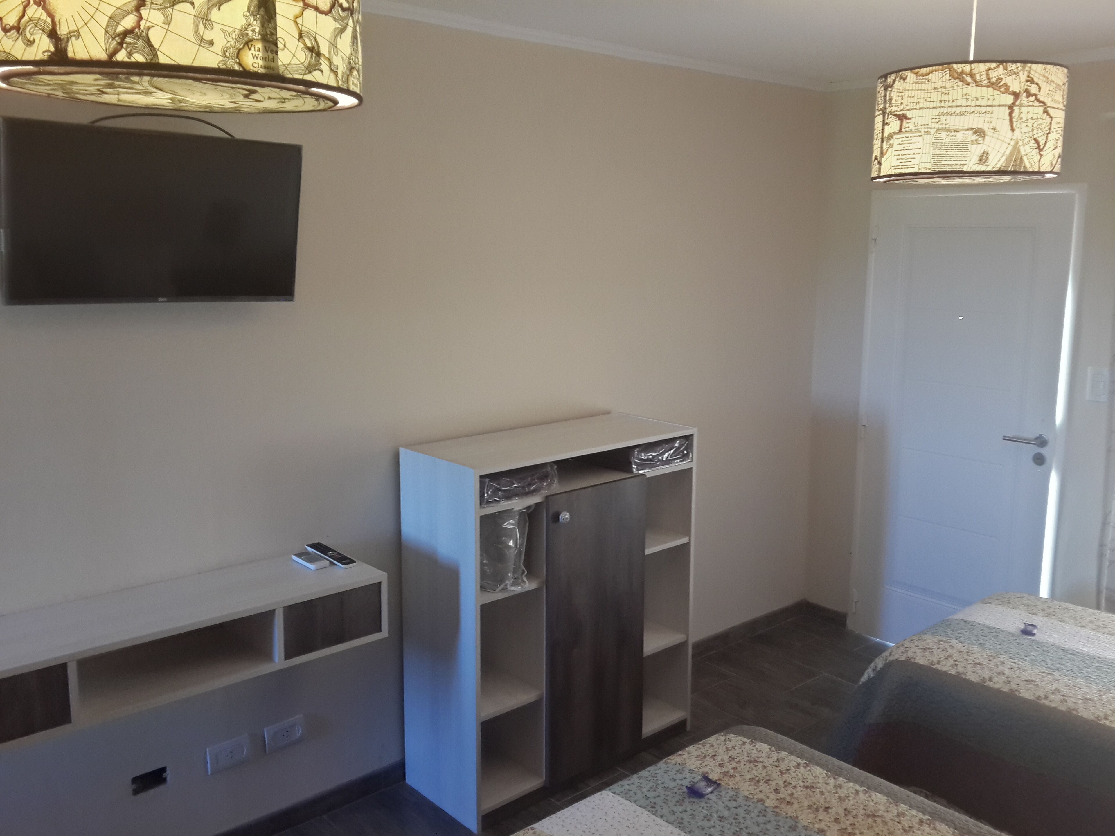A room with a flat-screen TV mounted on the wall, a built-in wardrobe, a door, and a patterned rug on the floor.