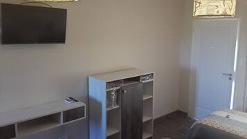 A room with a flat-screen TV mounted on the wall, a built-in wardrobe, a door, and a patterned rug on the floor.