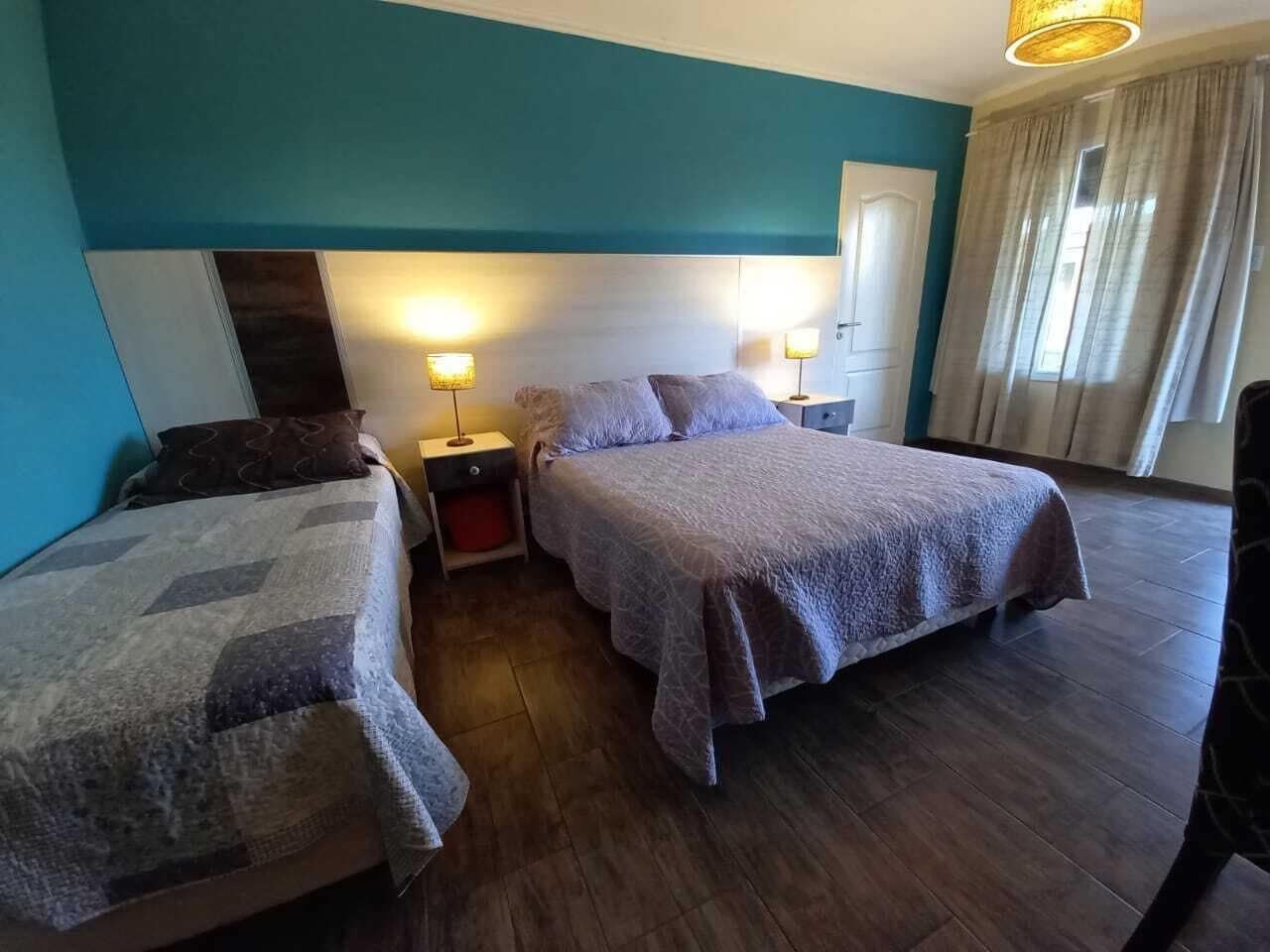 A hotel room with two beds, a nightstand with lamps, and a window with curtains.