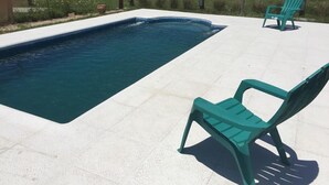 A swimming pool with two green chairs and a house in the background. - Altos de Adonai (Lonquimay)