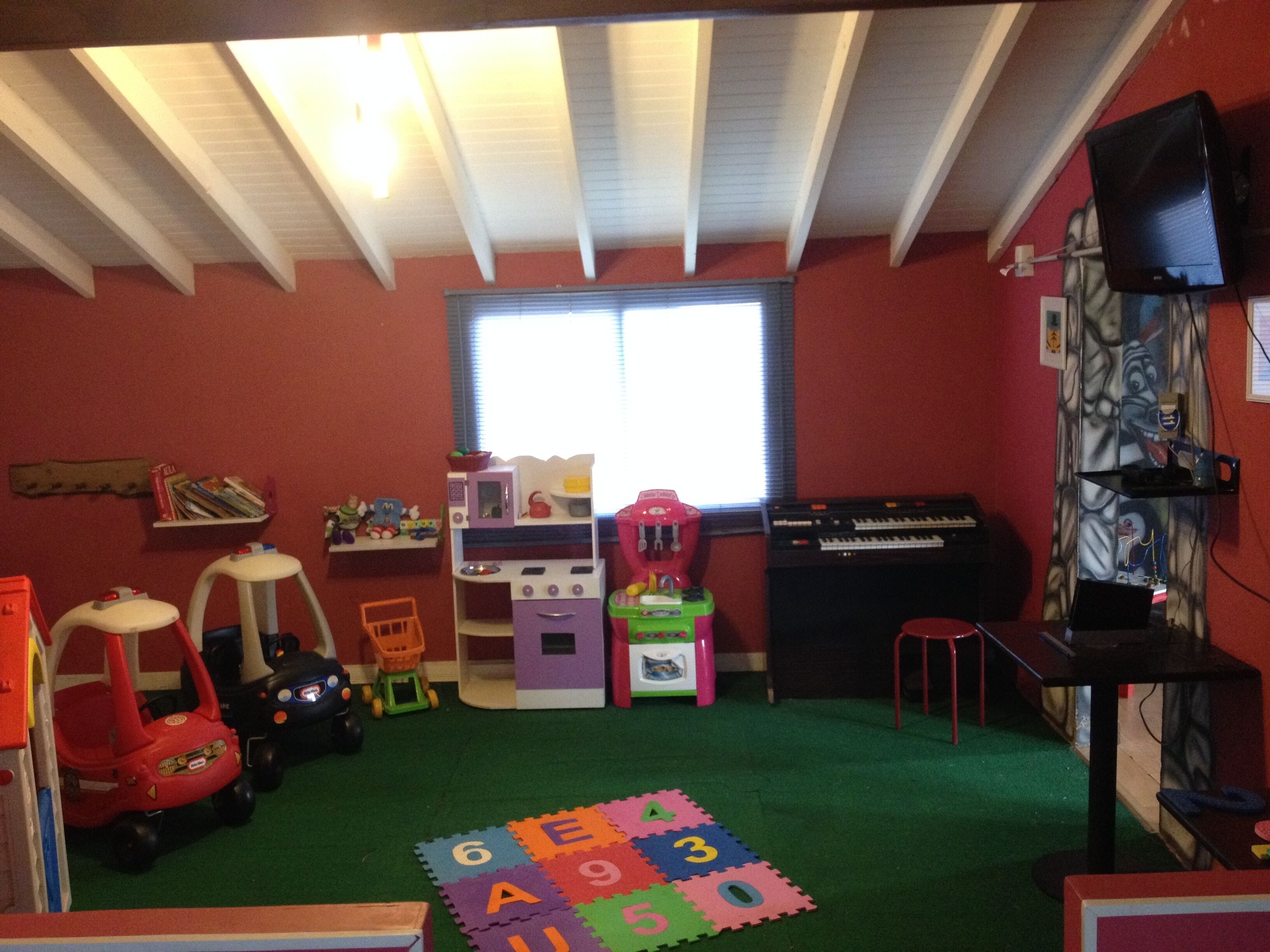 Ein Kinderzimmer mit grünem Teppich, einer Spielküche, Spielzeug und einem Klavier.