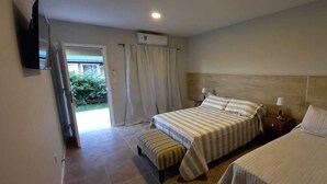 A bedroom with a bed, a bench, a nightstand, a TV, and a window with curtains. - Altos de Adonai (Lonquimay)