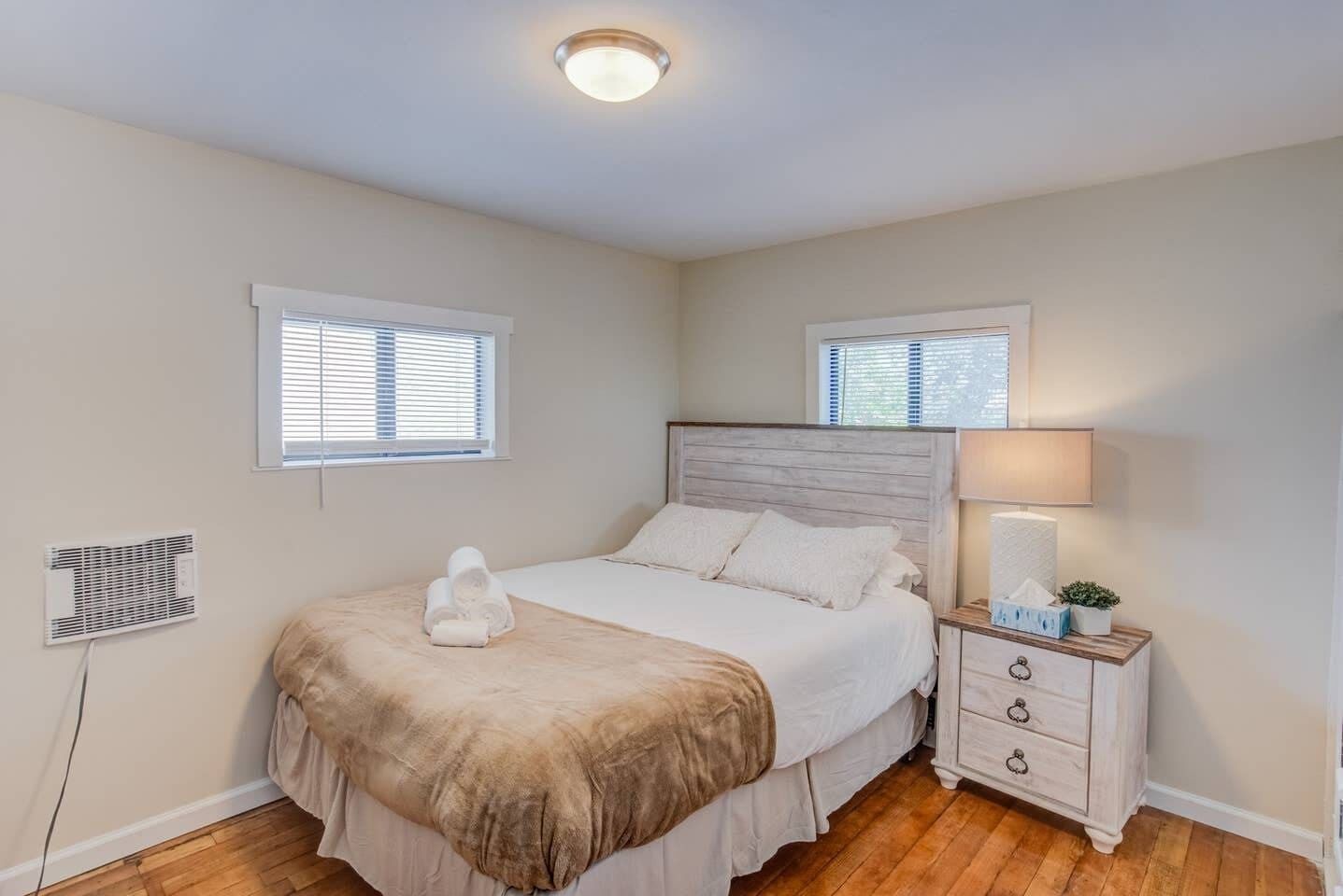 A bedroom with a bed, bedside table, and two windows.