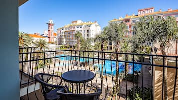 Un balcón con vista a una piscina, palmeras y edificios al fondo.
