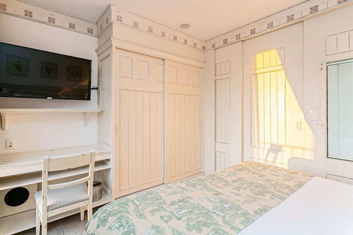 Un dormitorio con cama, escritorio, silla, armario y televisor.
