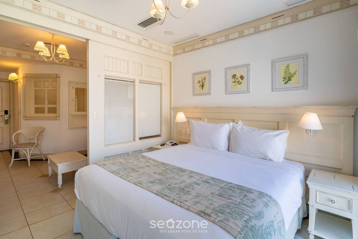 Una habitación de hotel con una cama grande, mesitas de noche, una silla y una ventana con contraventanas.