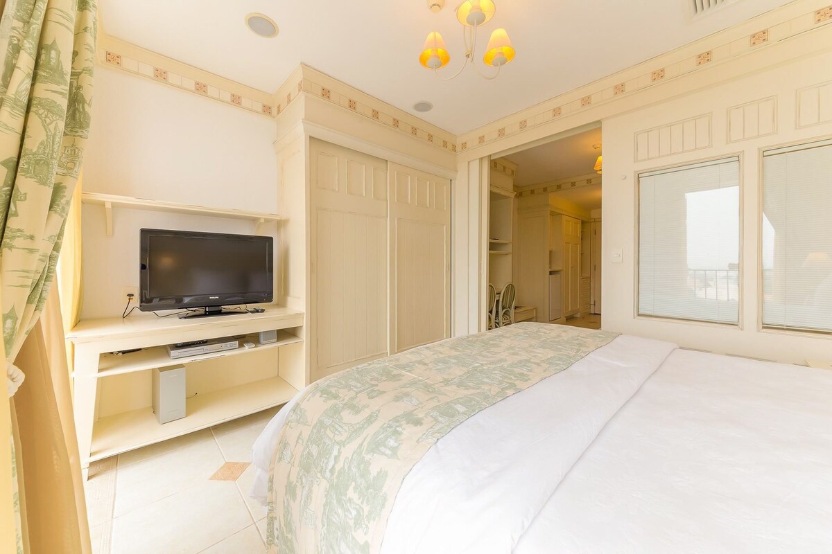 Habitación con cama, televisión, armario y baño a la vista a través de una puerta abierta.