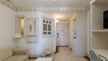 Una habitación con sofá, una silla, una mesa, televisor y una puerta que da a otra habitación.