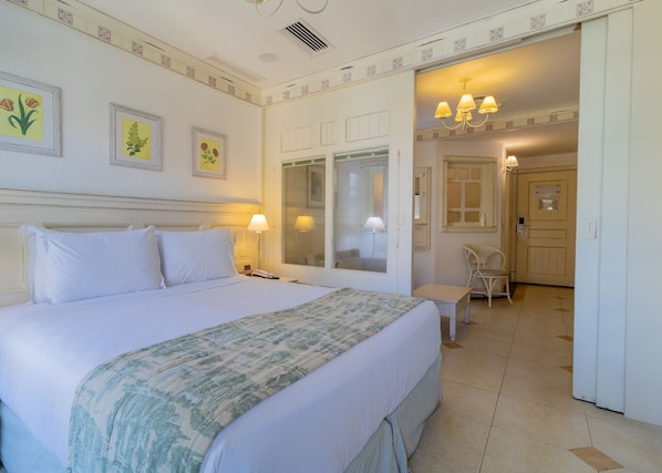 A hotel room with a bed, bedside lamps, a chair, a desk, and a door leading to another room.