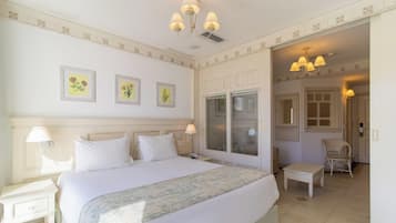 Een hotelkamer met een groot bed, een zithoek met een stoel en een deur naar een andere kamer.
