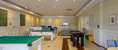 A room with multiple pool tables, a sofa, and a television.