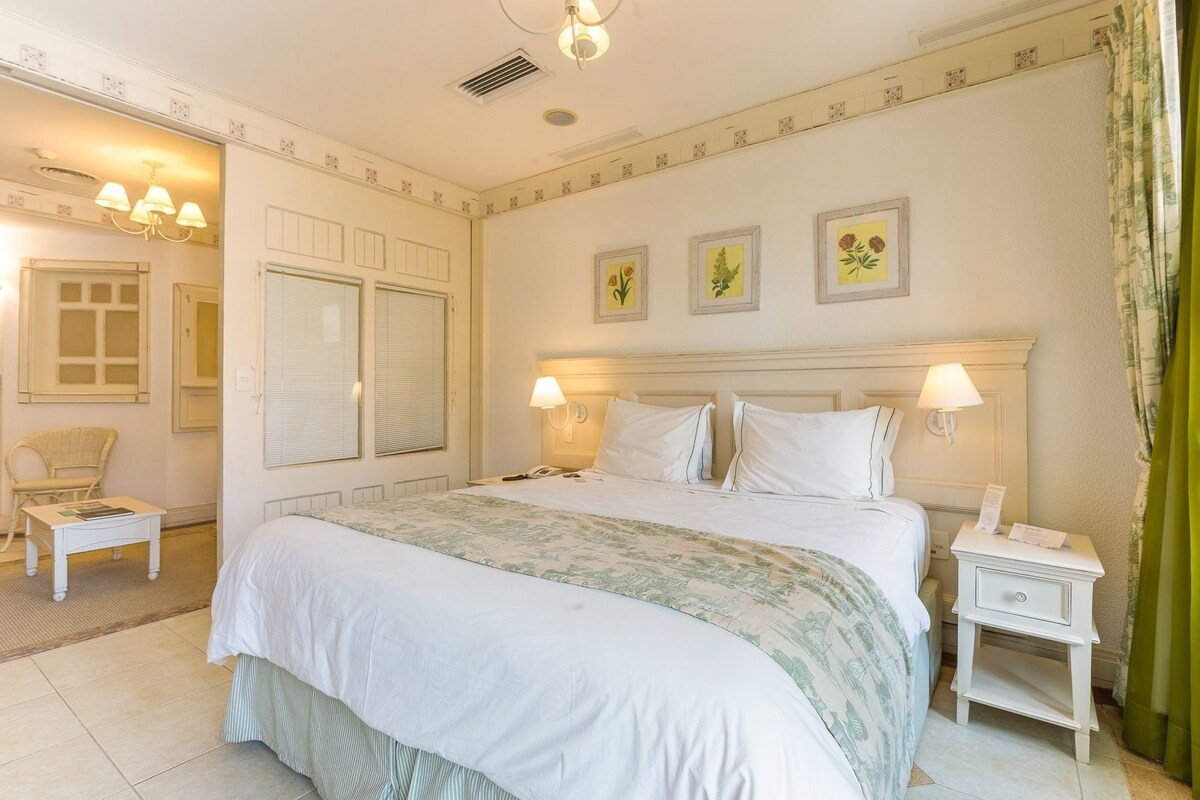 Un dormitorio ordenado con cama, mesitas de noche, una silla y lámparas de pared.