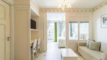 Une pièce comprenant un canapé, une table, une chaise, un téléviseur et une fenêtre avec des rideaux.