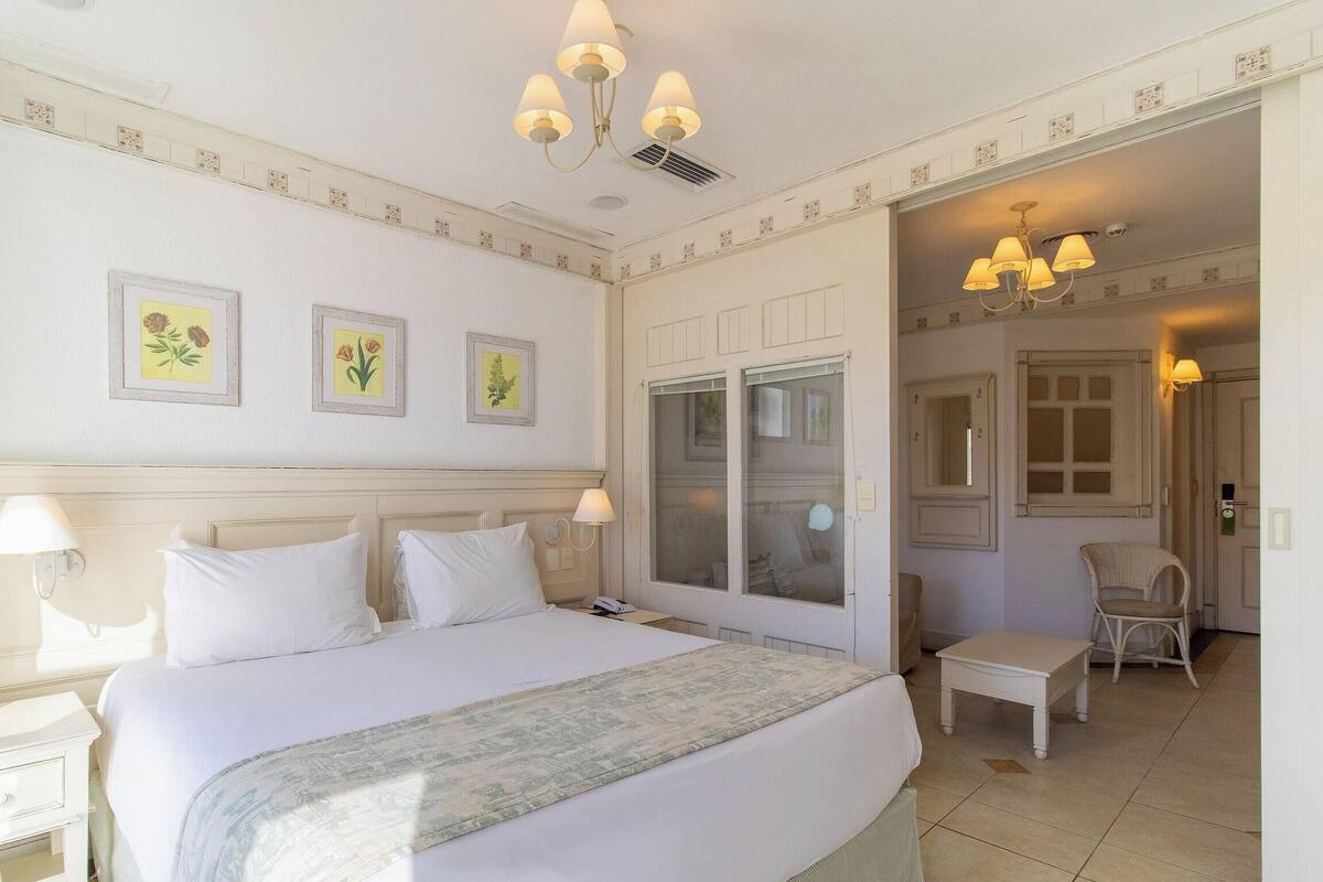 A hotel room with a large bed, bedside lamps, a wardrobe, a small table, and a chair.