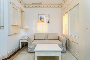 Una habitación con un sofá color crema, una mesa blanca, una lámpara y cuadros enmarcados en la pared.