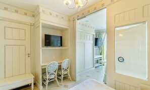 A room with a television on a shelf, two chairs, a bed, and a door leading to another room. - Confortáveis Studios no IL Campanario Resort ILCJR (Florianópolis)