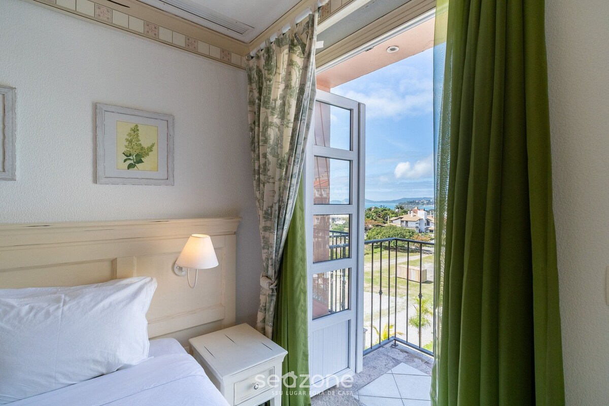 Habitación de hotel con cama, mesita de noche, lámpara de pared, un cuadro enmarcado y balcón con vistas.