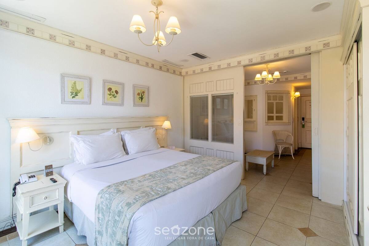 Una habitación de hotel con una cama, mesita de noche, lámpara y una silla en la esquina.