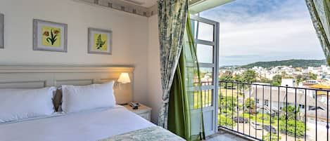 A hotel room with a bed, a nightstand, a lamp, two framed pictures, and a balcony with a view of the city.