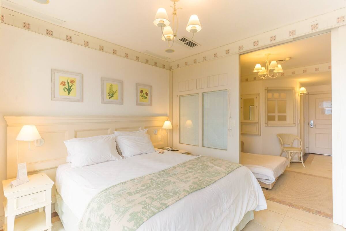 Habitación de hotel con una cama grande, lámparas de noche, mesita de noche, espejo y una silla.